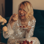 Woman in a sparkly dress laughing while eating cake.