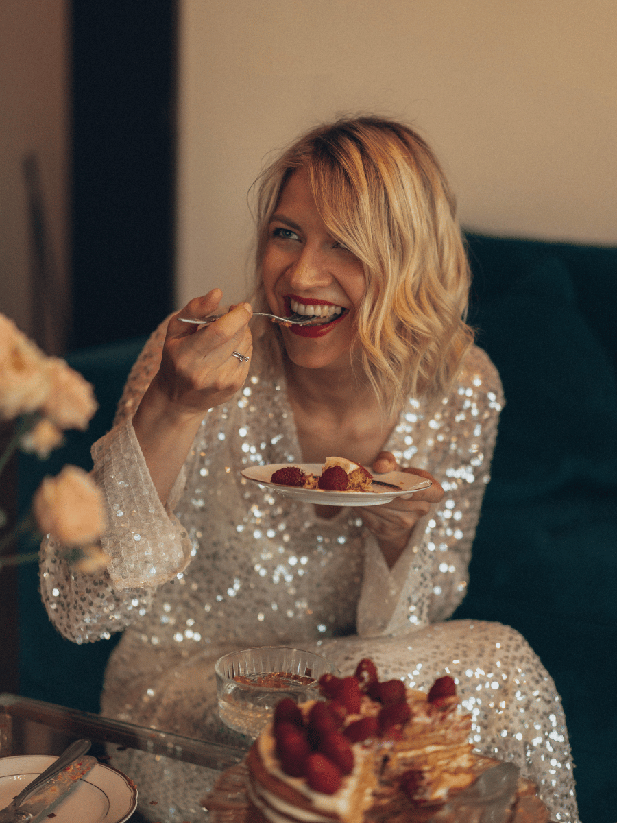 Woman in a sparkly dress laughing while eating cake.